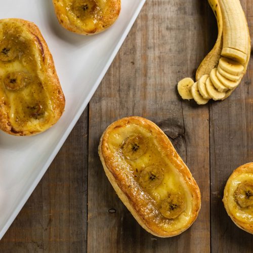 Bananitos | Pastelería Ciro Guatemala | Delicadas piezas de hojaldre horneado con mantequilla, rellenas de nuestro suave manjar de leche artesanal, coronadas con rodajas frescas de banano y un toque de mermelada de naranja que aporta una acidez equilibrada y brillante.
