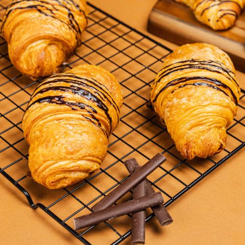 Croissant de chocolate | Pastelería Ciro Guatemala | Croissant artesanal elaborado con nuestra masa laminada especial a base de mantequilla importada, fermentado y horneado lentamente para lograr capas aireadas y doradas. Relleno con dos generosas barras de chocolate para un resultado indulgente en cada bocado.
